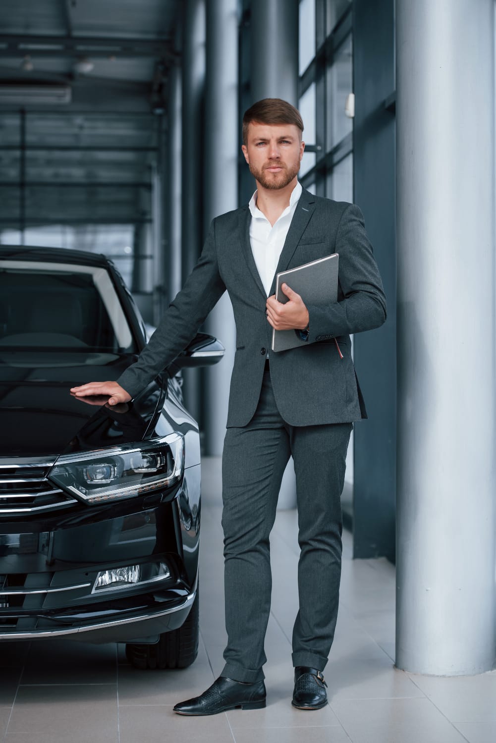 a man in a suit holding a notebook next to a car